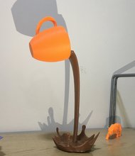 3D-Druck Symbolbild: orangene Tasse die braune Flüssigkeit ausschüttet, vor hellem Hintergrund