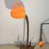 3D-Druck Symbolbild: orangene Tasse die braune Flüssigkeit ausschüttet, vor hellem Hintergrund